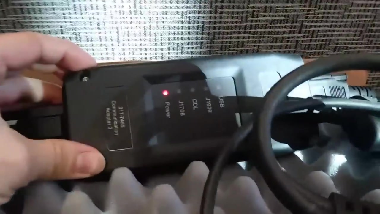 Close-up of a Cat Communication Adapter 3 with a red power light indicating it's on.