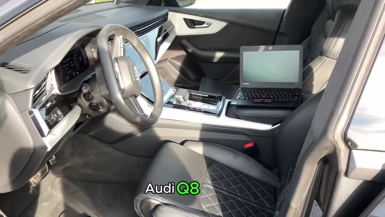 Interior of an Audi Q8 with a laptop on the passenger seat and a blue cable on the driver's side floor.